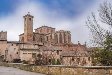 Obraz premium Scenic view of the rear facade of Siguenza Cathedral in Spain with its tall stone towers and gothic architecture rising above traditional old village houses under a dramatic cloudy sky