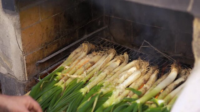 Detailed shot of a chef blowing on the fire and rearranging traditional Catalan cal&ccedil;ots as they cook on a grill with fire and smoke at a traditional outdoor barbecue in Catalonia, Spain.