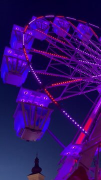 Vertical night shot of a Ferris wheel with vibrant neon light transitions.