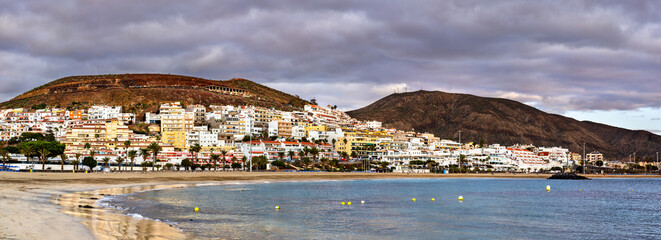 Scenic morning view of the sandy shoreline, calm ocean waters, and resorts of Playa de las Vistas in Playa de las Americas against a mountainous backdrop in Tenerife. © Leonid Andronov