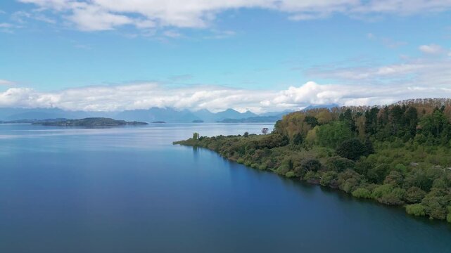 Ascending shot revealing calm lake shoreline with islands and Andean peaks. Lago Ranco, Chile