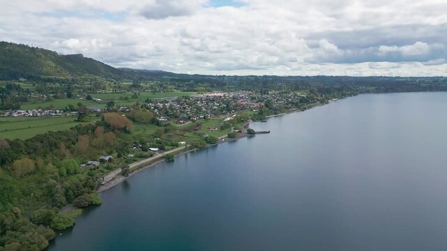 Aerial view of lakeside town along calm shoreline with forested hills. Lago Ranco, Chile