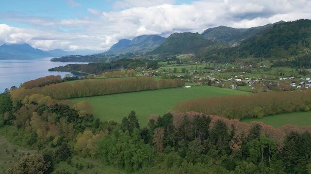 Panoramic pan over green fields and lakeside village with Andean backdrop. Lago Ranco, Chile