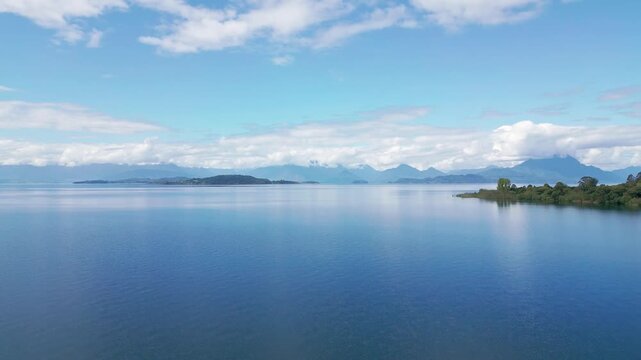 Descending shot over mirror-like lake with islands and snow-capped Andean peaks. Lago Ranco, Chile