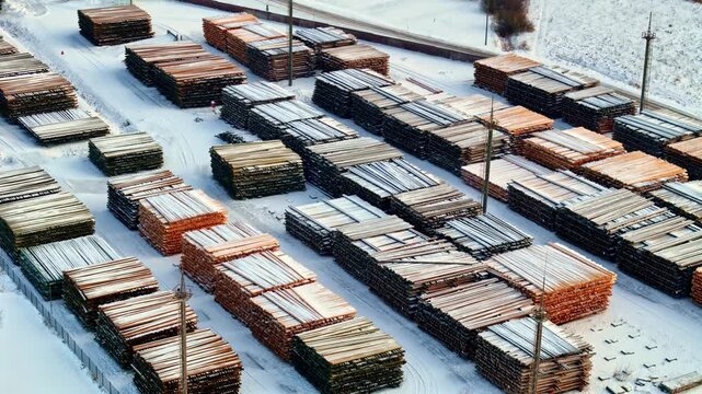 Elevated view of stacked timber and wooden planks arranged in rows across a snow covered lumber yard