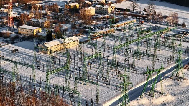 Snow covered electrical substation with steel lattice structures and power lines in winter sunlight