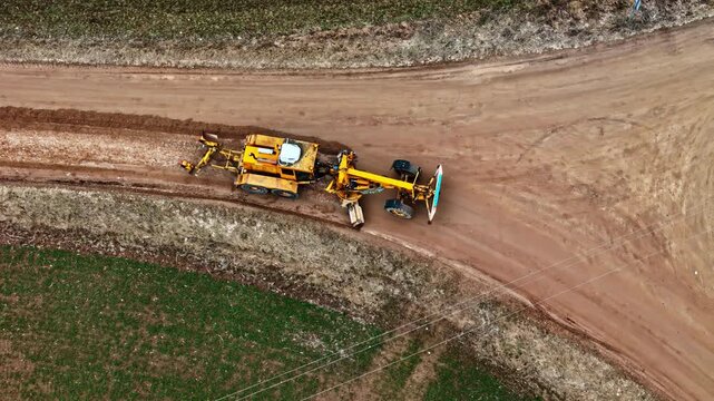 Top drone view over a tractor with a land leveler constructing a road.