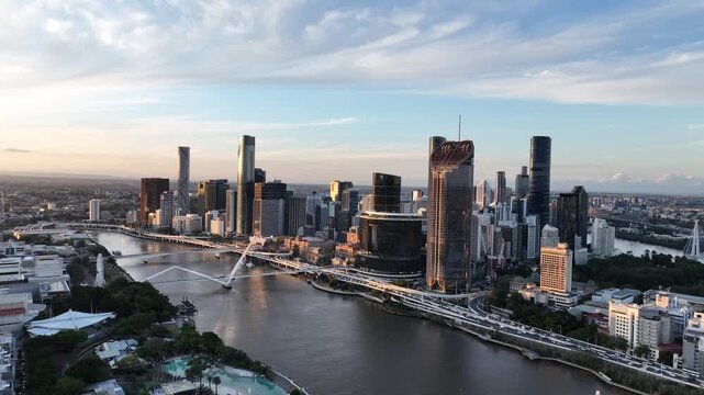 Slow drone orbit at golden hour over the Brisbane River, circling Queens Wharf and The Star Brisbane towers with Neville Bonner Bridge and a CityCat ferry in view, Brisbane, QLD, Australia