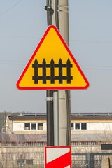 Przejazd kolejowy z zaporami, trójkątny znak ostrzegawczy z czerwonym obramowaniem i żółtym tłem, rogatka na znaku. © Henryk Guziak