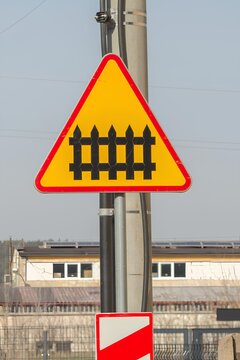 Przejazd kolejowy z zaporami, tr&oacute;jkątny znak ostrzegawczy z czerwonym obramowaniem i ż&oacute;łtym tłem, rogatka na znaku.