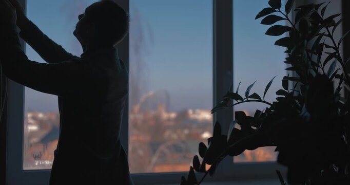 A man in a classic suit closes the blinds on a window