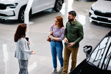 Couple discussing car options with saleswoman in showroom