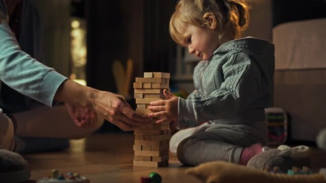 Young daughter and her mother are engrossed in warm evening play session, constructing wobbly tower with wooden Jenga blocks on floor, combining fun and learning through interactive play and balance