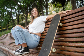 Fototapeta premium Young woman relaxing on park bench with skateboard