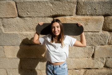 Young woman smiling carrying skateboard on shoulder © Jorge