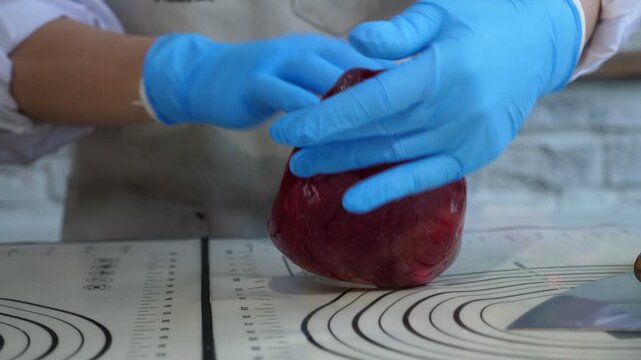 A pastry chef carefully mixes and kneads the soft, stretchy red caramel in their craft pastry shop, creating handmade lollipops and other sweets.