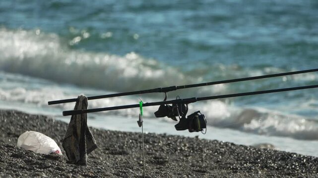 Fishing rods seashore, waiting patiently for a catch by the blue ocean waves on a sunny pebble beach.