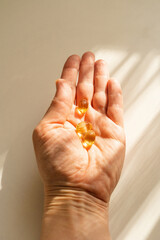 Close-up of woman's hand holding capsules with nutritional supplements, warm sunlight. A healthy...