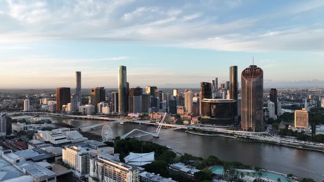 Slow drone orbit at golden hour along the Brisbane River, featuring Queens Wharf and The Star Brisbane towers with Neville Bonner Bridge and the CBD skyline, Brisbane, QLD, Australia