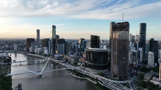 Slow drone pan right at golden hour along the Brisbane River, showcasing Queens Wharf and The Star Brisbane towers with Neville Bonner Bridge and the CBD skyline, Brisbane, QLD, Australia