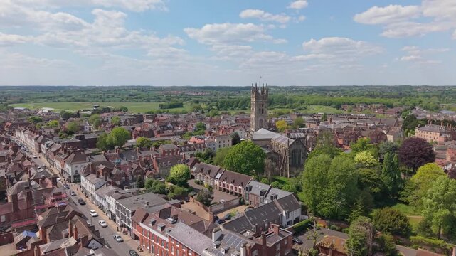Orbiting footage of Warwick village with St Mary&rsquo;s Church at the center, captured on a sunny spring day with white clouds decorating the sky.