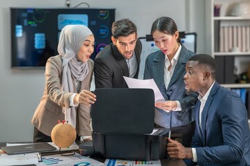 Fototapeta premium A group of four business people are gathered around a printer, looking at a document that has just been printed. They are all smiling and appear to be happy and excited.