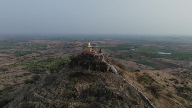 Aerial drone orbits a Hindu temple with a golden spire perched on a rocky hilltop surrounded by the vast arid Deccan plateau near Garwad in Solapur Maharashtra