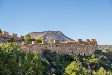 Fototapeta premium The ancient stone wall of Roman-era fortresses in Cartagena, Spain, rises majestically against the backdrop of a rugged mountain, the historic strength and enduring beauty