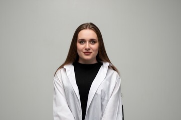 Fototapeta premium Young woman with long brown hair wearing white shirt and black top, glancing at camera in studio portrait