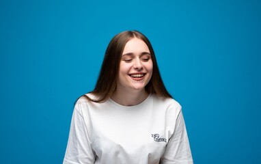 Obraz premium Young woman with closed eyes laughing, expressing joy, happiness, and cheerfulness on a blue background