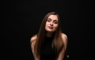 Fototapeta premium Young woman with long brown hair posing confidently in a studio portrait with a dark background