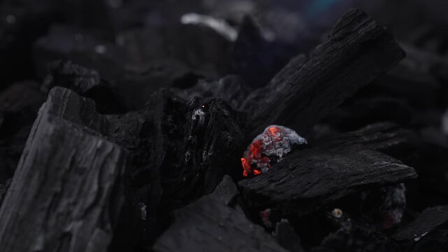 Close up of a blue gas burner flame lighting charcoal, with glowing embers and ash in a dark grill setup. Concept of ignition, heat, cooking, fuel, and energy.