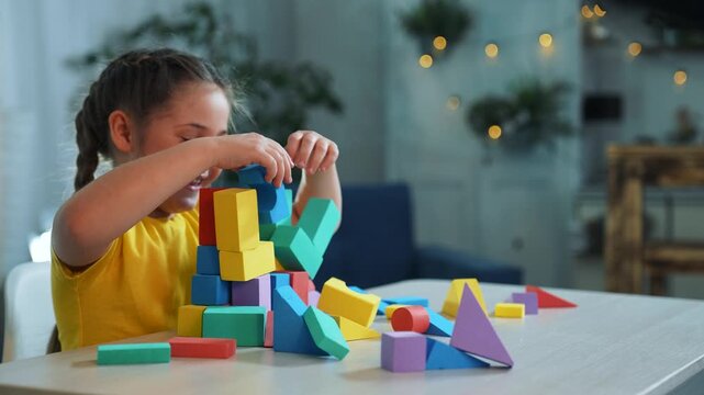 Girl stacking colorful block tower on table in cozy living room while focused on play and learning with toy shape and color exploration and fine motor skill practice by child building design