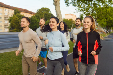 Group of runners jogging marathon in summer city park. Smiling friends team running along road during morning fitness training, outdoors sport exercise, healthy energy and strong teamwork of athletes