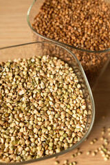 Obraz premium Green and brown buckwheat in glass jars on kitchen table top view. Close-up of gluten-free grains, healthy food and diet concept. Organic buckwheat for cooking, superfood