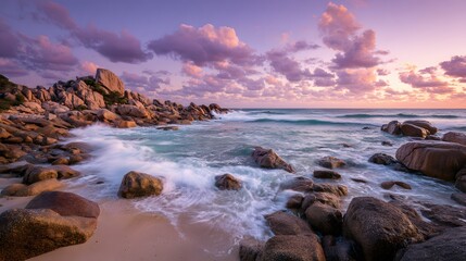 Fototapeta premium Dramatic coastal landscape displays massive granite boulders on a sandy beach, where foamy ocean waves crash beneath a pastel sunset sky.