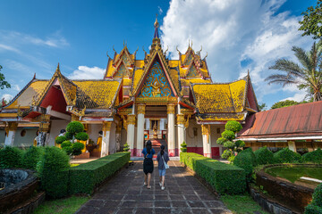 Fototapeta premium Beautiful golden temple entrance with ornate gable and yellow tile roof at Wat Wang Wiwekaram in Sangkhlaburi, Kanchanaburi, Thailand with mother and daughter walking along garden path