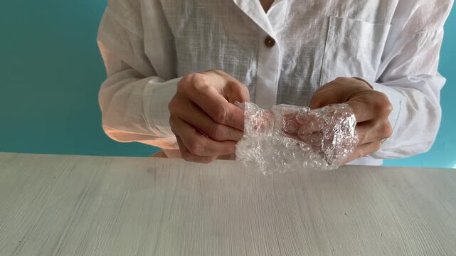hands squeezing and popping transparent bubble wrap used for shipping protection, tactile stress relief action with sharp popping sounds and packaging material texture