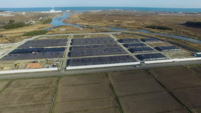 Aerial footage of Fukushima decontamination soil storage site in Japan. Thousands of contaminated soil units are under black tarps, organized in rectangular blocks.