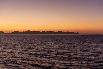 Obraz premium Sunset as seen from the sea, with the coastline trailing in the distance.
