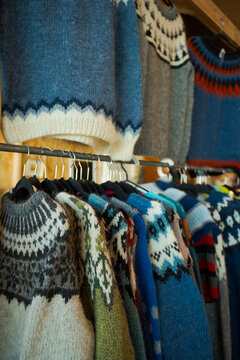 Colorful Icelandic wool sweaters hanging by a window with intricate Nordic patterns.