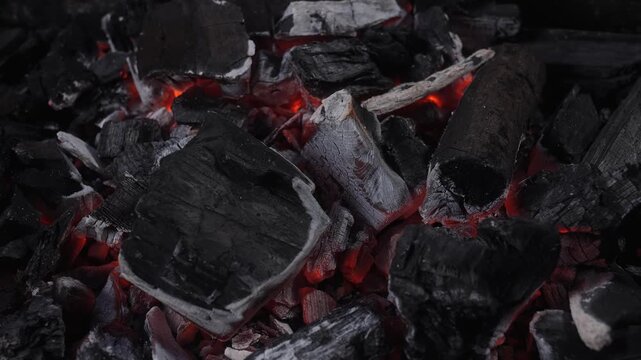 Close up of smoldering charcoal with glowing embers and ash texture in low light, ideal for fire, heat, grilling, fuel, and dramatic background concepts.