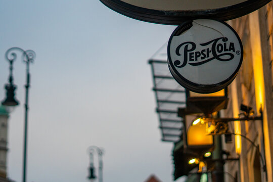 Vintage Pepsi-Cola sign on a historic building wall, urban evening lighting with street lamps, retro advertising in the city, twilight cityscape with nostalgic branding.