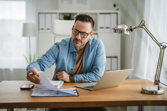 Man wearing eyeglasses checking business paperwork at home office