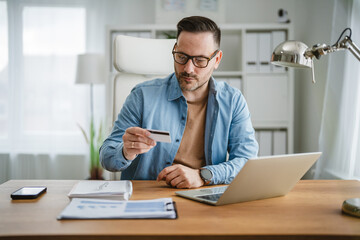 Fototapeta premium Happy man shopping online with credit card at home