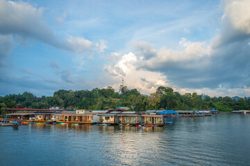 Obraz premium Peaceful floating house and colorful kayak on tranquil river with mountain backdrop under dramatic sky in Sangkhlaburi, Kanchanaburi, Thailand