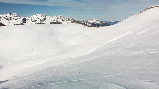 Vast mountain slope crossed by ski tracks - Pullback aerial move