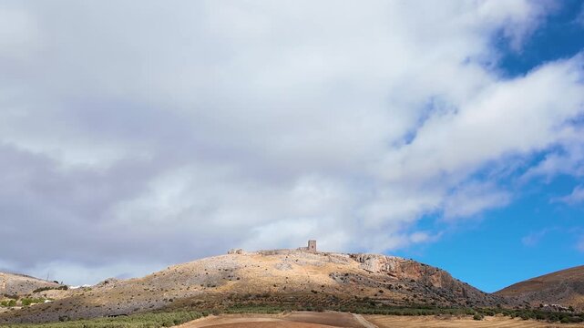 Static aerial timelapse of the Castillo de la Estrella castle in Teba, Spain, showing moving cloud shadows over the hill and fortress under a blue sky.