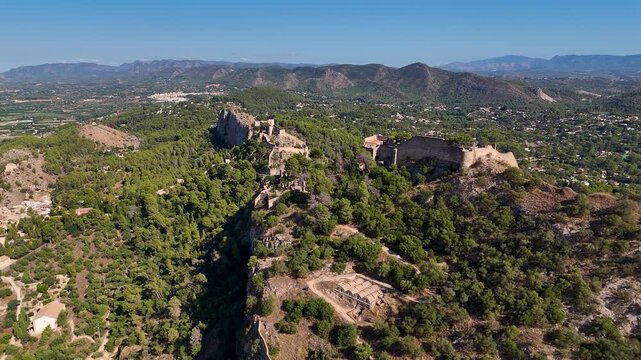 Aerial drone flying backward and rising over the historic Xativa Castle in Valencia, Spain, revealing its medieval walls on a mountain ridge.