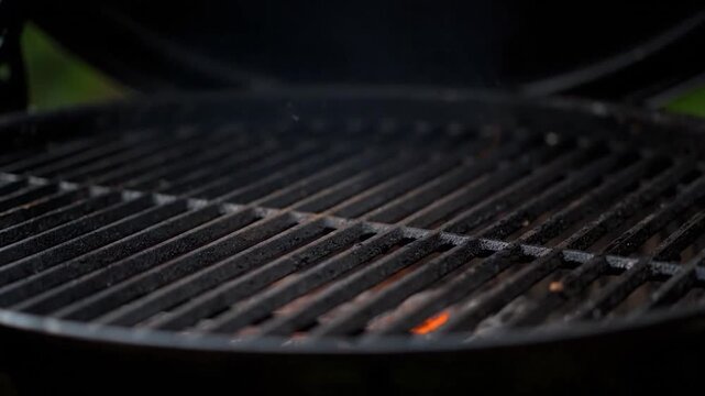 Close-up of a dark, used grill with a metal grate and visible embers. Smoke rises